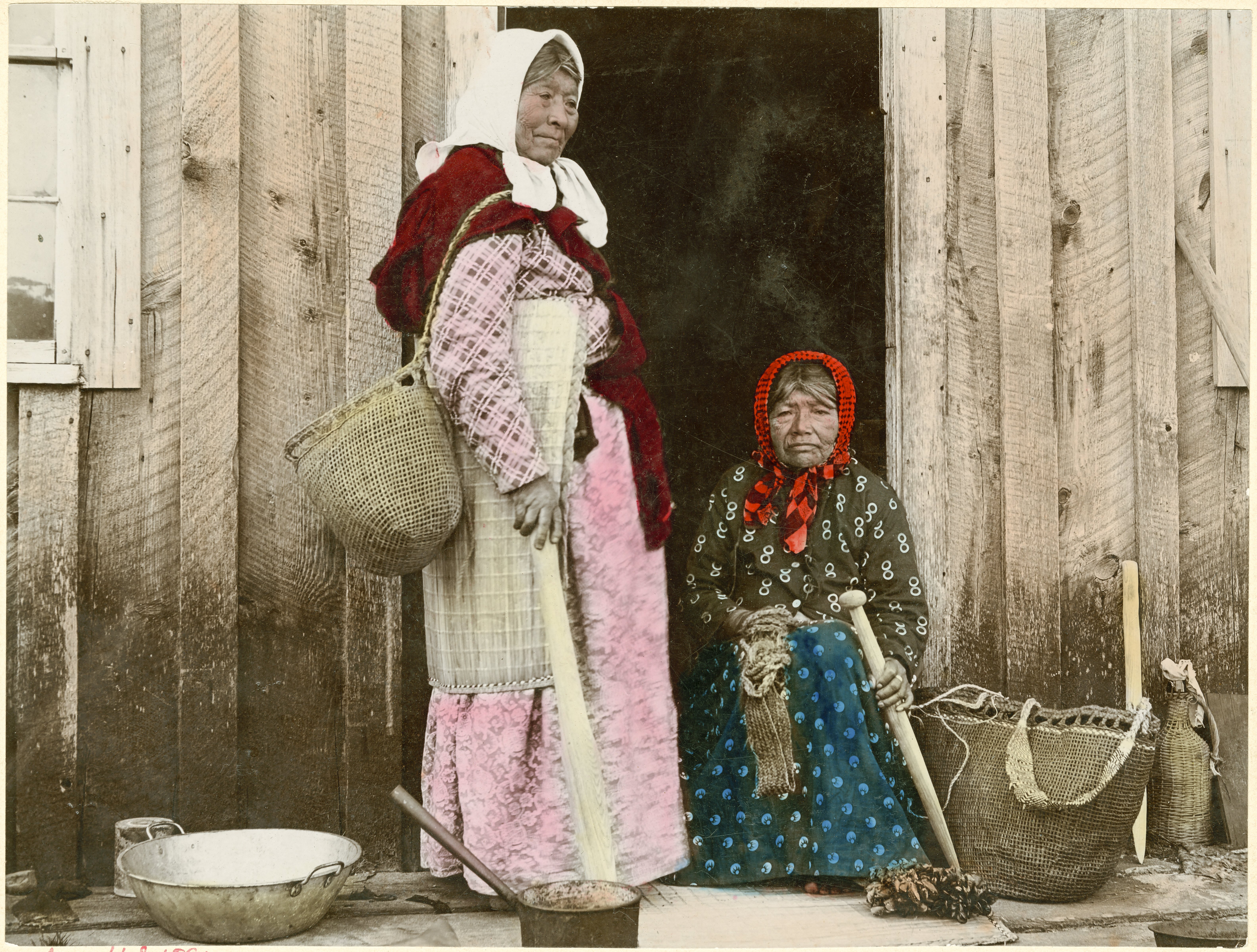 Tsin-is-tum stands in front of an Indian Place house; the woman seated is likely De-o-so, wife of Chief Kotata.