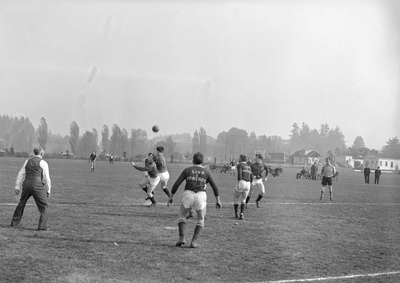 Players for the Albina Engine & Machine Works soccer team, the Subchasers, on a field during a game against a team for Lind & Pomeroy. The ball can be seen in the air, with blurry players underneath