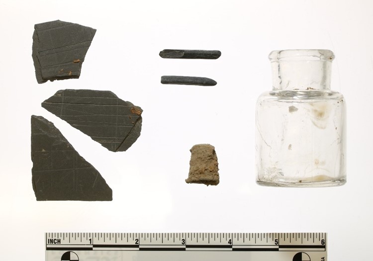 Slate tablet fragments (left); pencil fragments (top center); a thimble (bottom center); and an ink bottle (right) found during the 2021 archaeological investigations at the OSH North Campus.