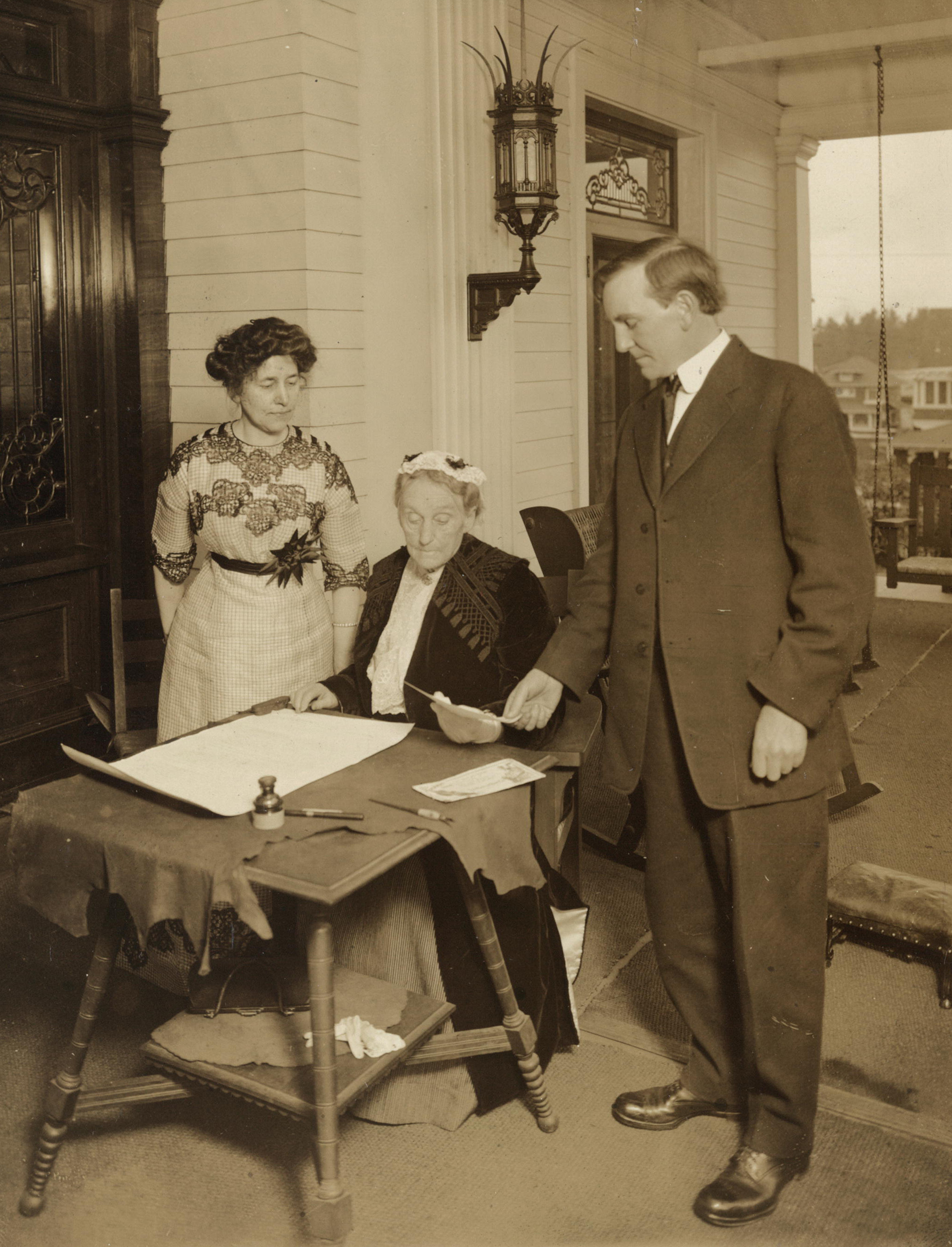 Abigail Scott Duniway (seated) signing first Equal Suffrage Proclamation, Nov. 1912, with Governor Oswald West (r) and Dr. Viola M. Coe (l).
