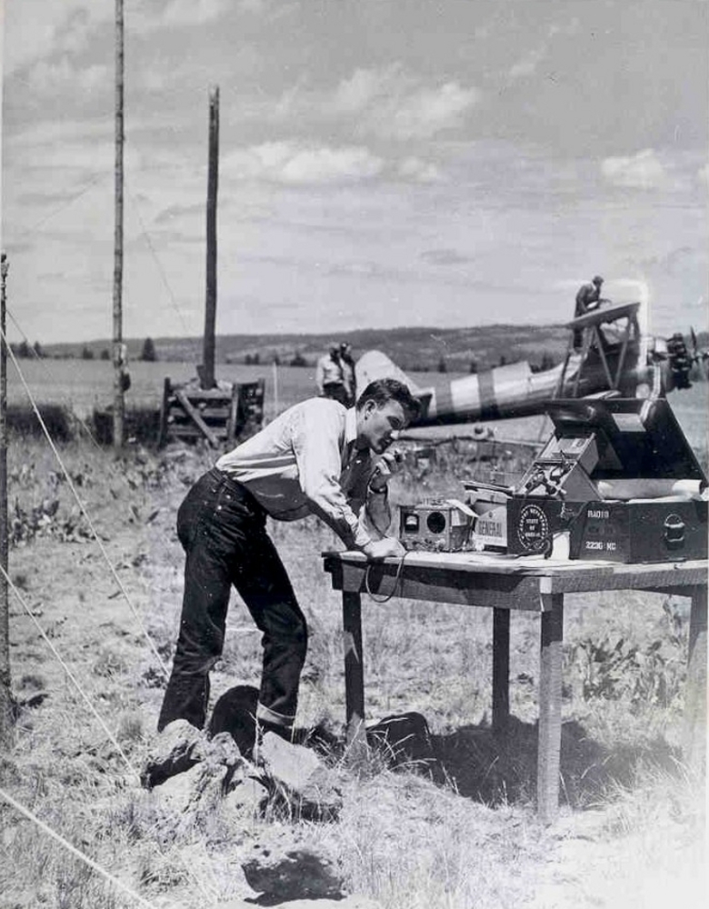 Oregon forestry staffer in the early 1950s talking into commercial VHF radio; a 1936 USFS Radio Lab type SPF radio is also on the table.